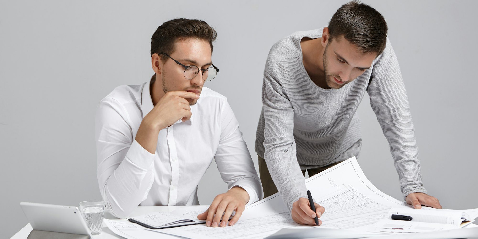 Portrait of two creative arhitects sit at workplace, discuss house project, look attentively at blue